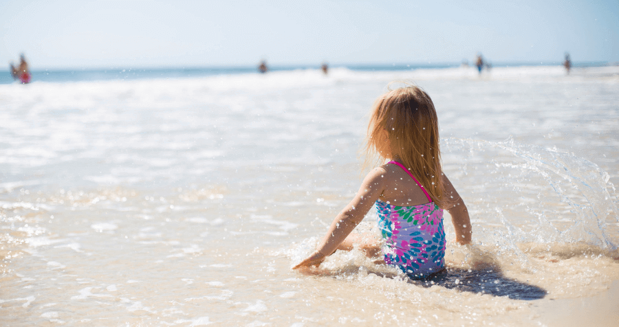 Co zabrać nad morze z dzieckiem – dziewczynka siedząca na brzegu morza, bawiąca się w wodzie